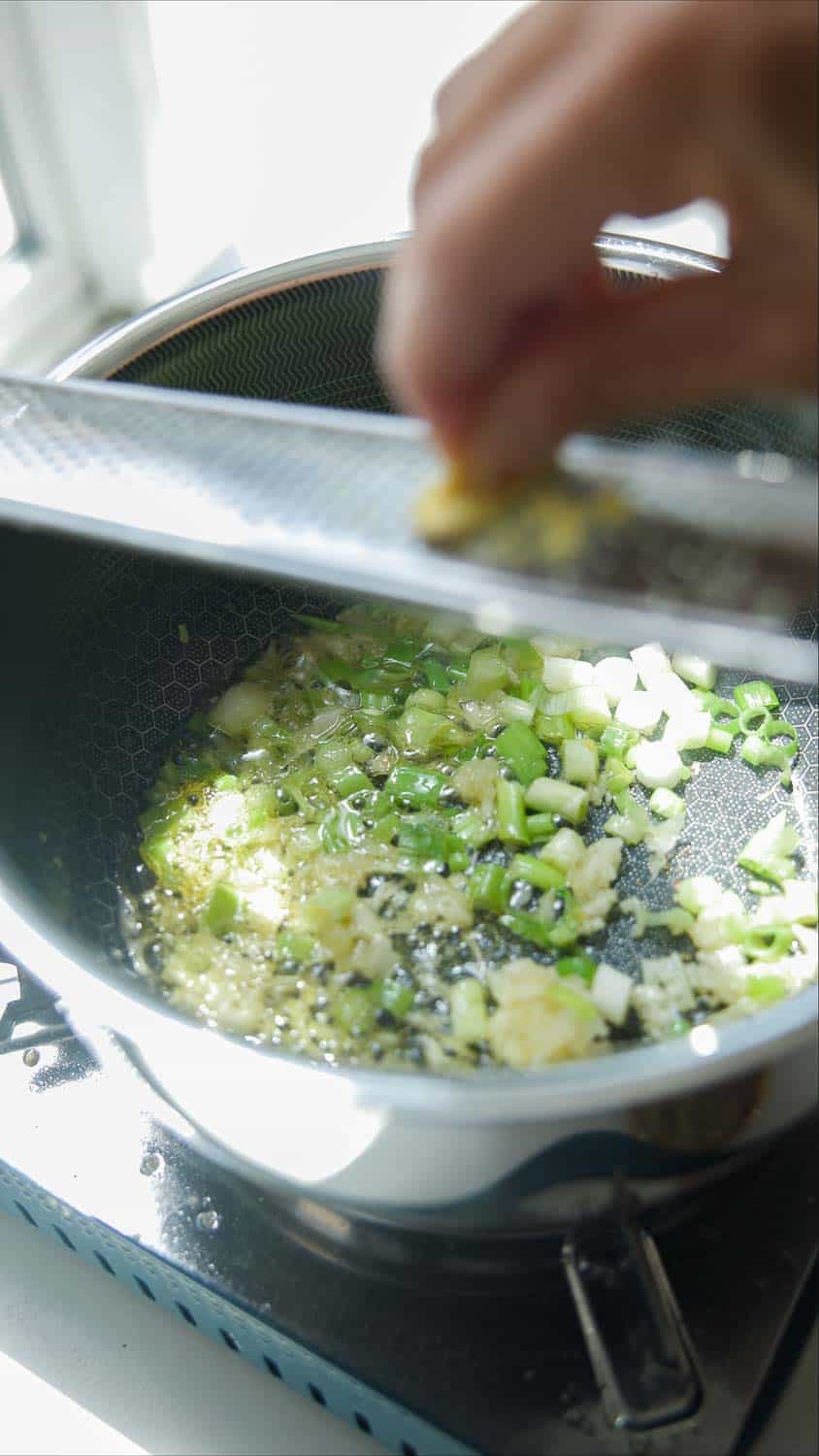 grating ginger into pot of scallions and garlic and oil